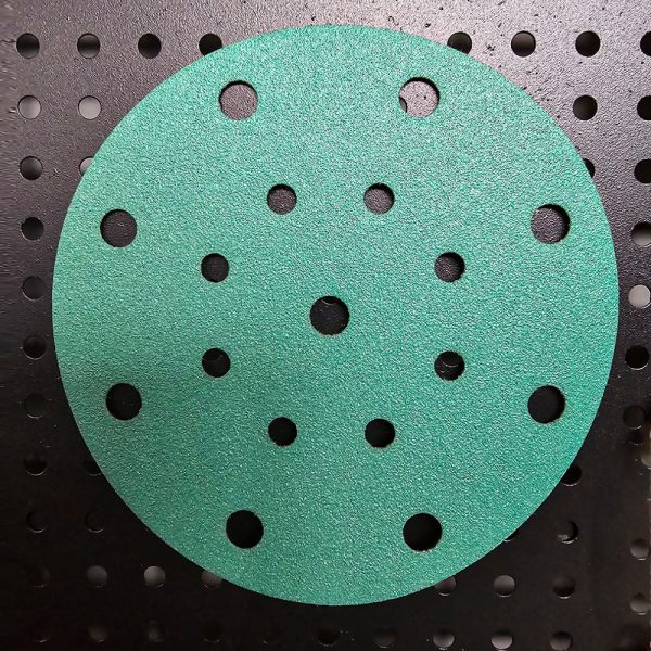 A green velcro sanding disc featuring multiple holes for efficient dust extraction during sanding tasks.